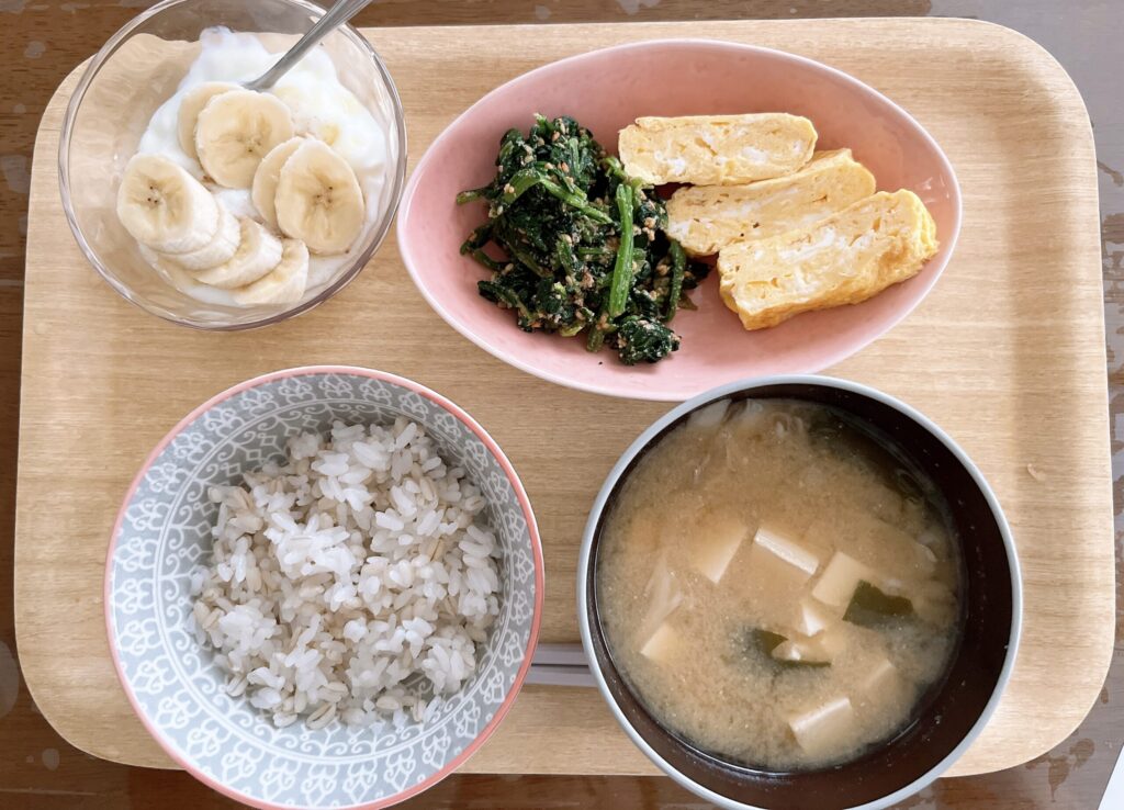もち麦ごはん、味噌汁、だし巻き卵、ほうれん草のごま和え、ヨーグルト、バナナ半分の朝食の写真